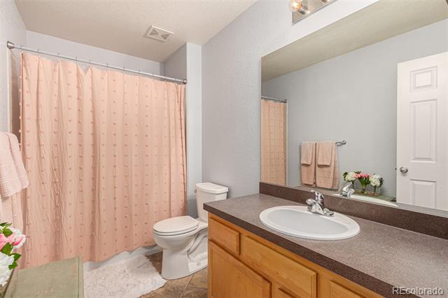 Bathroom with a wood vanity and oval sink beside a pink patterned shower curtain.