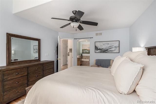 Bedroom with a large white bed, dark wood dresser and mirror, and ceiling fan.