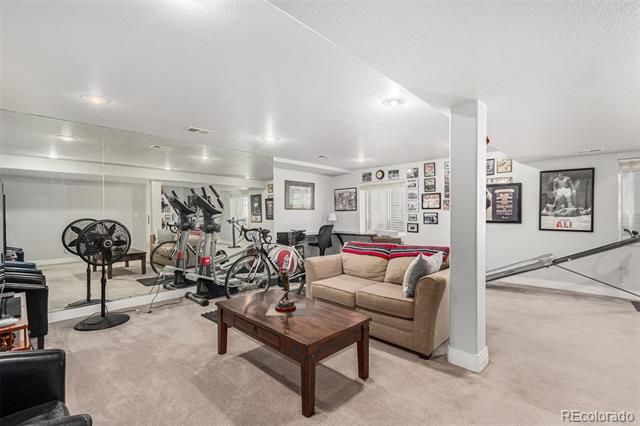 Basement recreation room with exercise equipment, a mirrored wall, and a beige sofa.