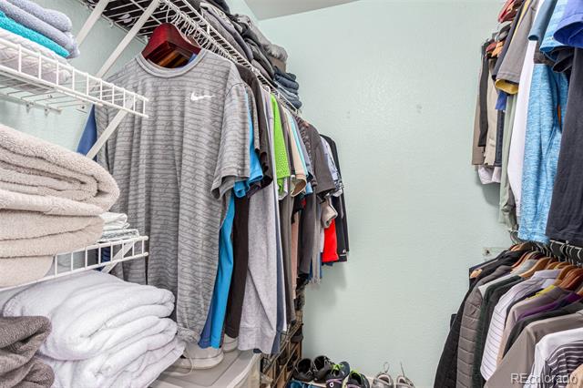 Walk-in closet with hanging clothes, folded towels on shelves, and shoes on the floor.