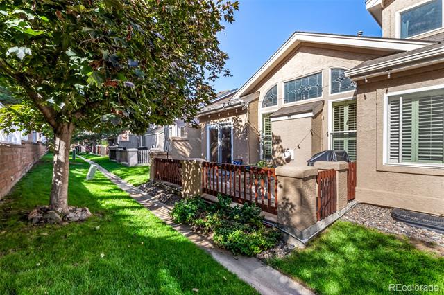 House exterior with a fenced patio, green lawn, mature tree, and large arched windows.
