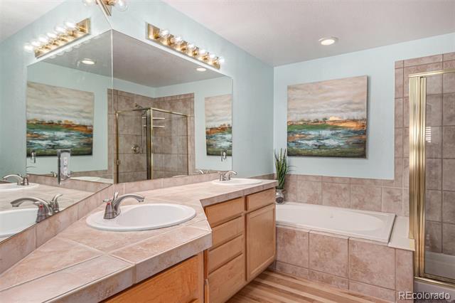 Bathroom with double vanity, large mirror, tiled bathtub surround, and landscape artwork.