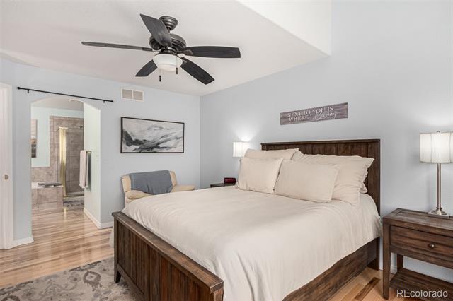 Bedroom with white bedding, dark wood furniture, ceiling fan, and an open bathroom doorway.
