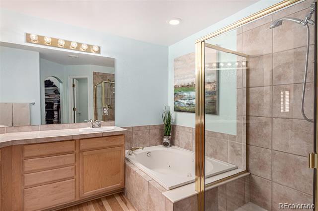 Bathroom with a wood vanity, corner soaking tub, and glass-enclosed tiled shower.