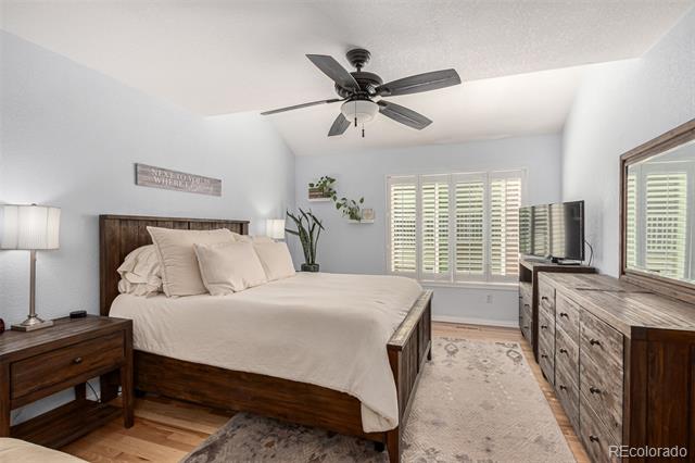 Bedroom with a dark wood bed, white bedding, plantation shutters, and a ceiling fan.
