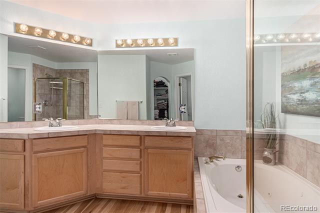 Bathroom with a double-sink wood vanity and corner soaking tub behind glass.