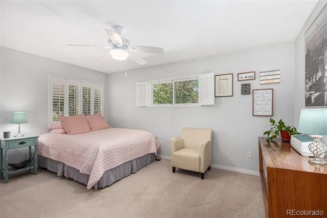 Furnished bedroom with a pink quilted bed, plantation shutters, and a beige armchair.