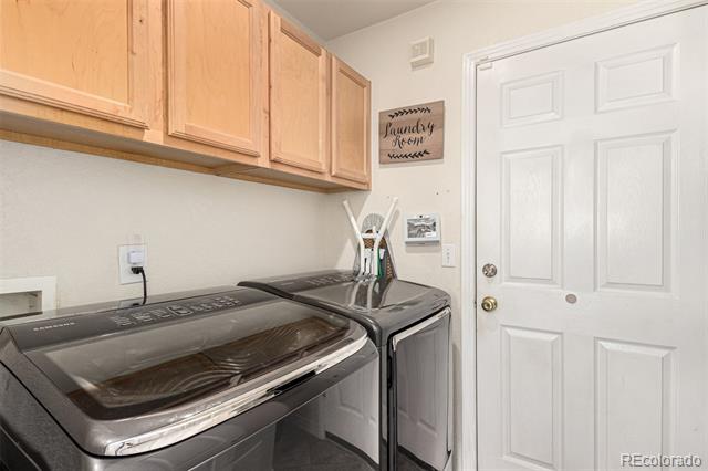 Laundry room with a washer and dryer beneath light wood cabinets beside a white paneled door.