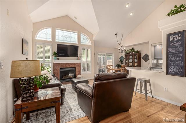 Living room with a fireplace, vaulted ceiling, and tall arched windows with white shutters.