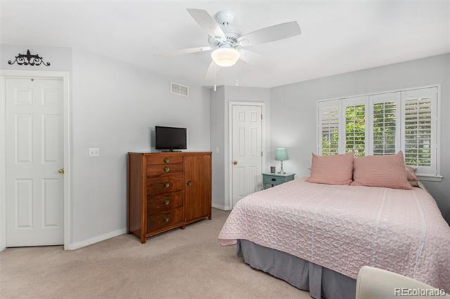 Bedroom with a pale pink quilted bed, wooden dresser, plantation shutters, and ceiling fan.