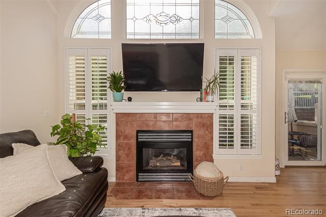 Living room with tiled fireplace, television, arched windows, and plantation shutters.