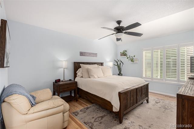 Bedroom with a dark wood bed, white bedding, cream armchair, and wide shuttered windows.