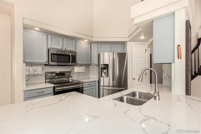 Kitchen with gray cabinets, stainless appliances, and a large veined quartz island with sink.