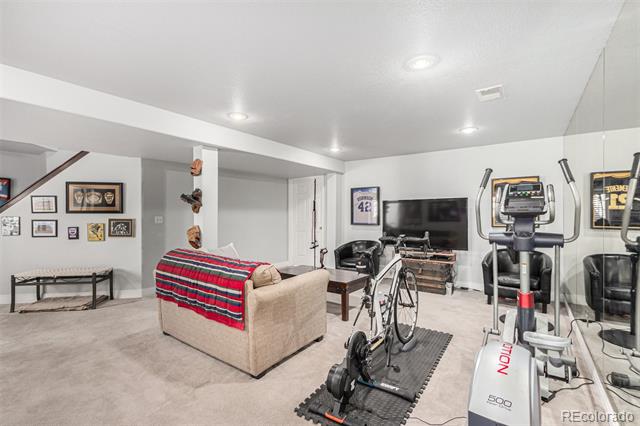 Basement recreation room with a striped-blanket sofa, television, sports memorabilia, and exercise equipment.