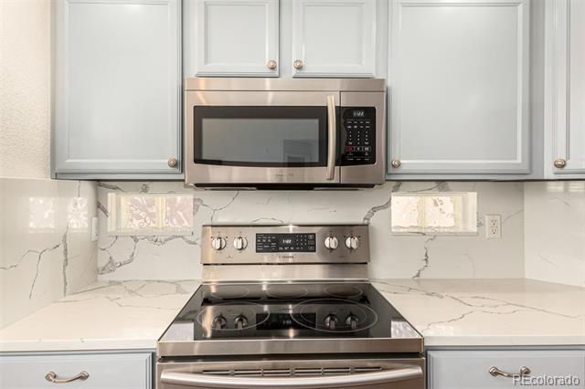 Kitchen with white cabinets, stainless steel appliances, and gray-veined countertops and backsplash.
