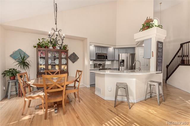 Open-plan dining area and kitchen with a white island, gray cabinets, and a wooden table beneath a chandelier.