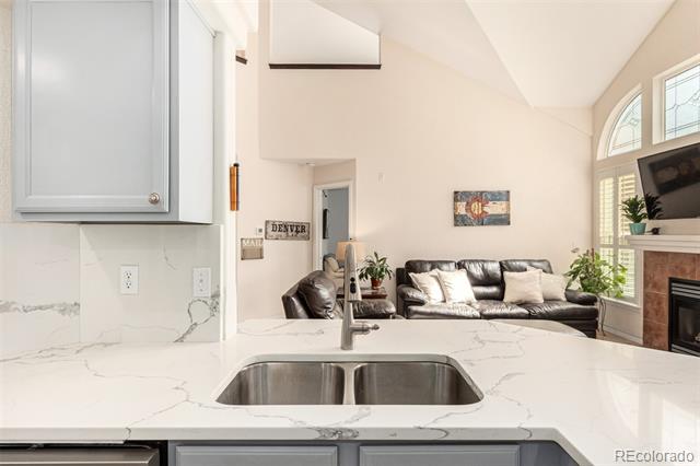 Open kitchen with a veined stone island overlooking a vaulted living room and fireplace.