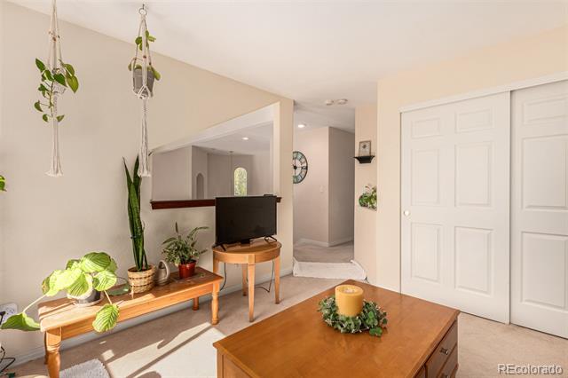 Furnished living room with a wooden coffee table, television, hanging plants, and white sliding closet doors.