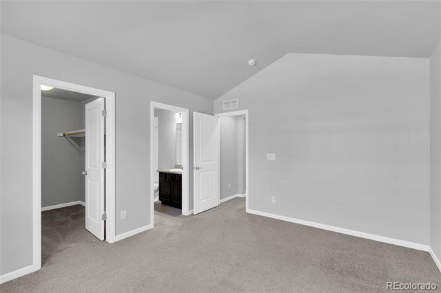 Empty bedroom with beige carpet, an open closet, and a bathroom vanity visible through the doorway.