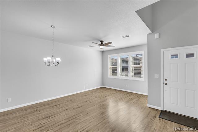 Empty living room with light wood flooring, a ceiling fan, and a window with blinds.
