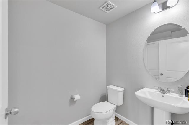 Bathroom with a white toilet, wall-mounted sink, and large round mirror.