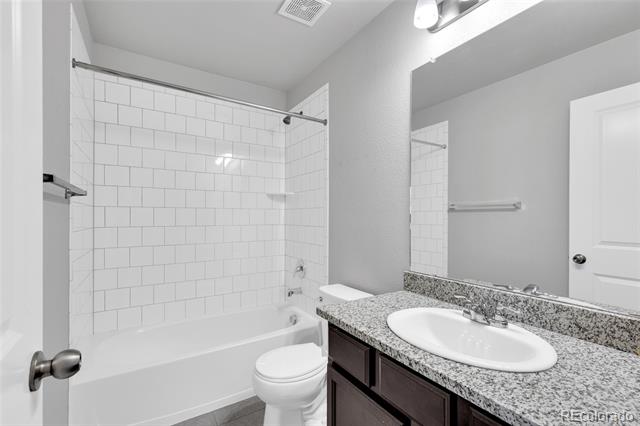 Bathroom with a white tiled tub and shower, toilet, and granite-topped dark wood vanity.