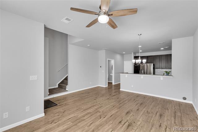 Open living and dining area with wood-look flooring, ceiling fan, dark kitchen cabinets, and a staircase.