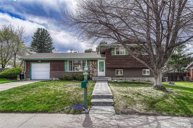 Brown split-level house with green trim, an attached garage, and a large leafless tree in the front yard.