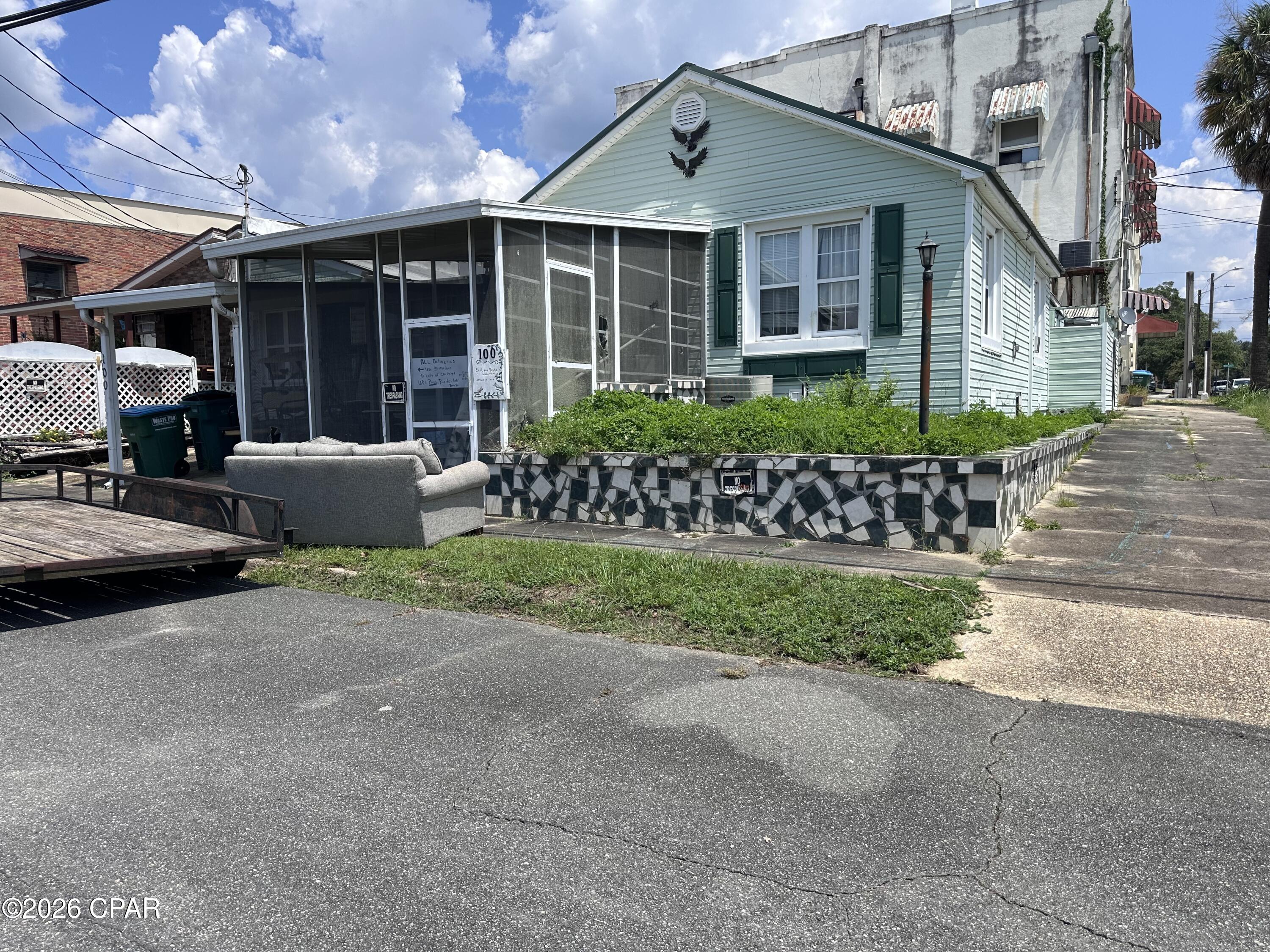 Pale green house with a screened porch and mosaic-tiled garden bed beside the street.