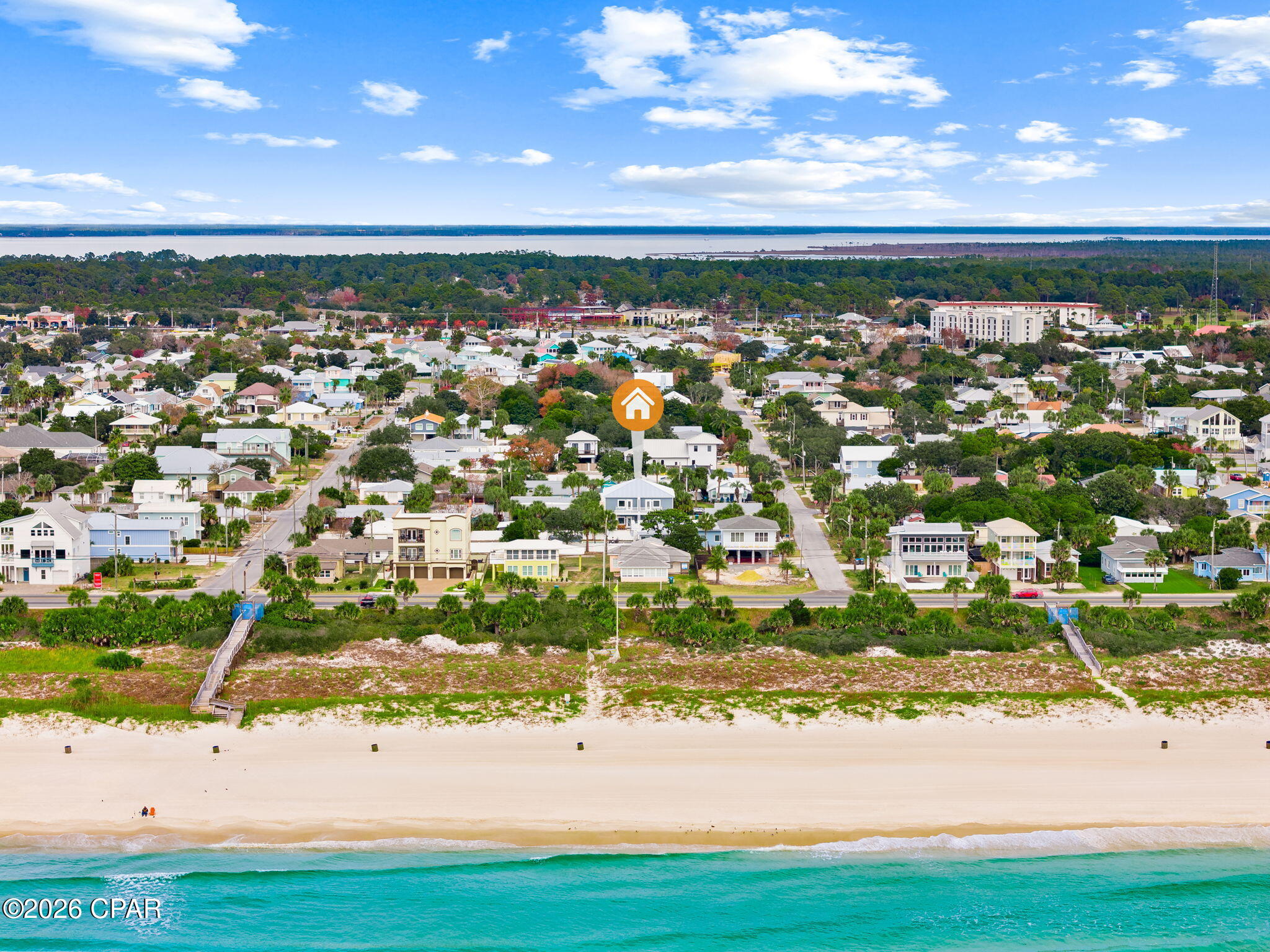 Aerial coastal neighborhood with the listed property marked, between a sandy beach and distant water.