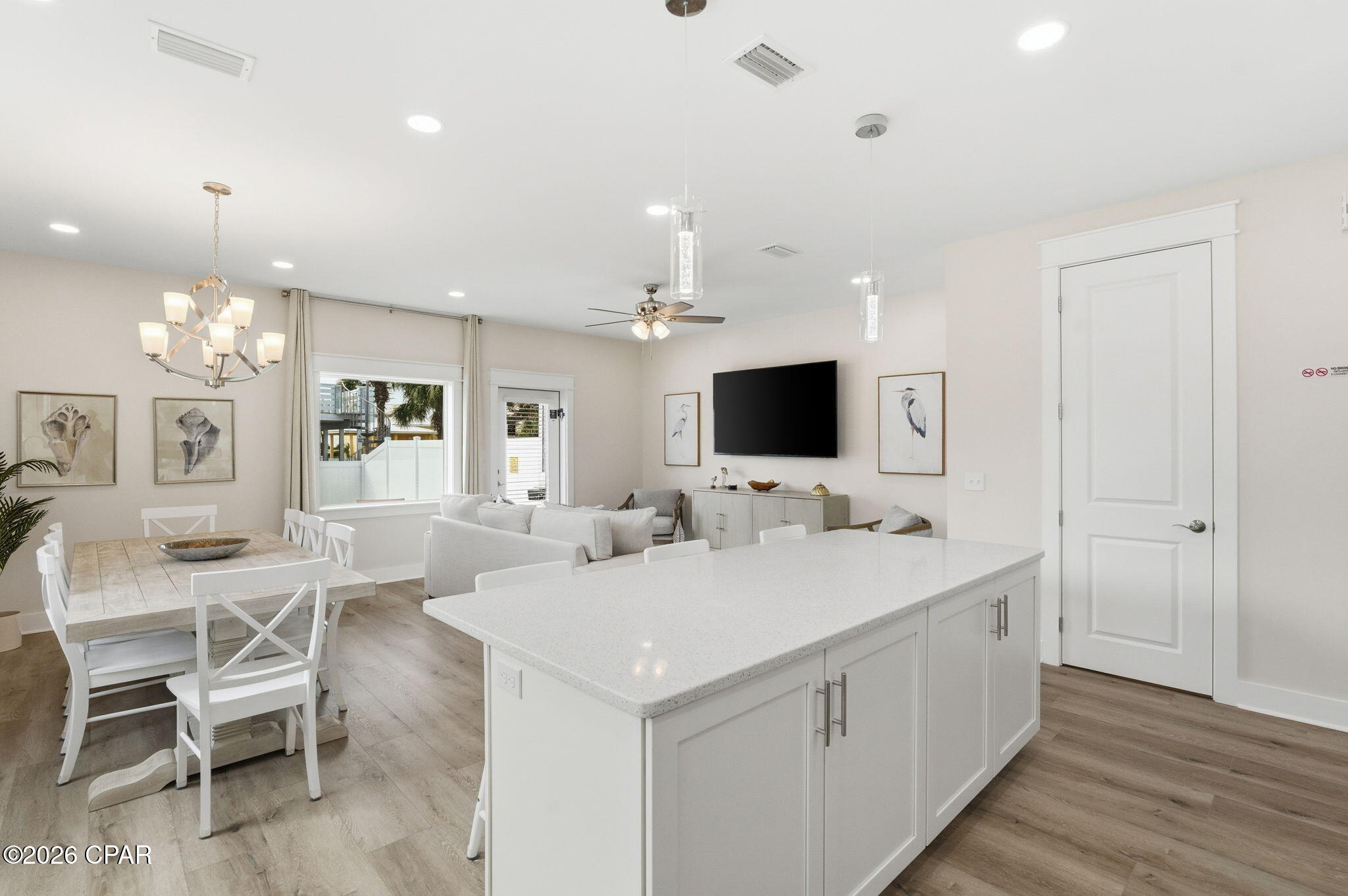Open-plan kitchen and living area with a large white island, dining table, and wood-look flooring.