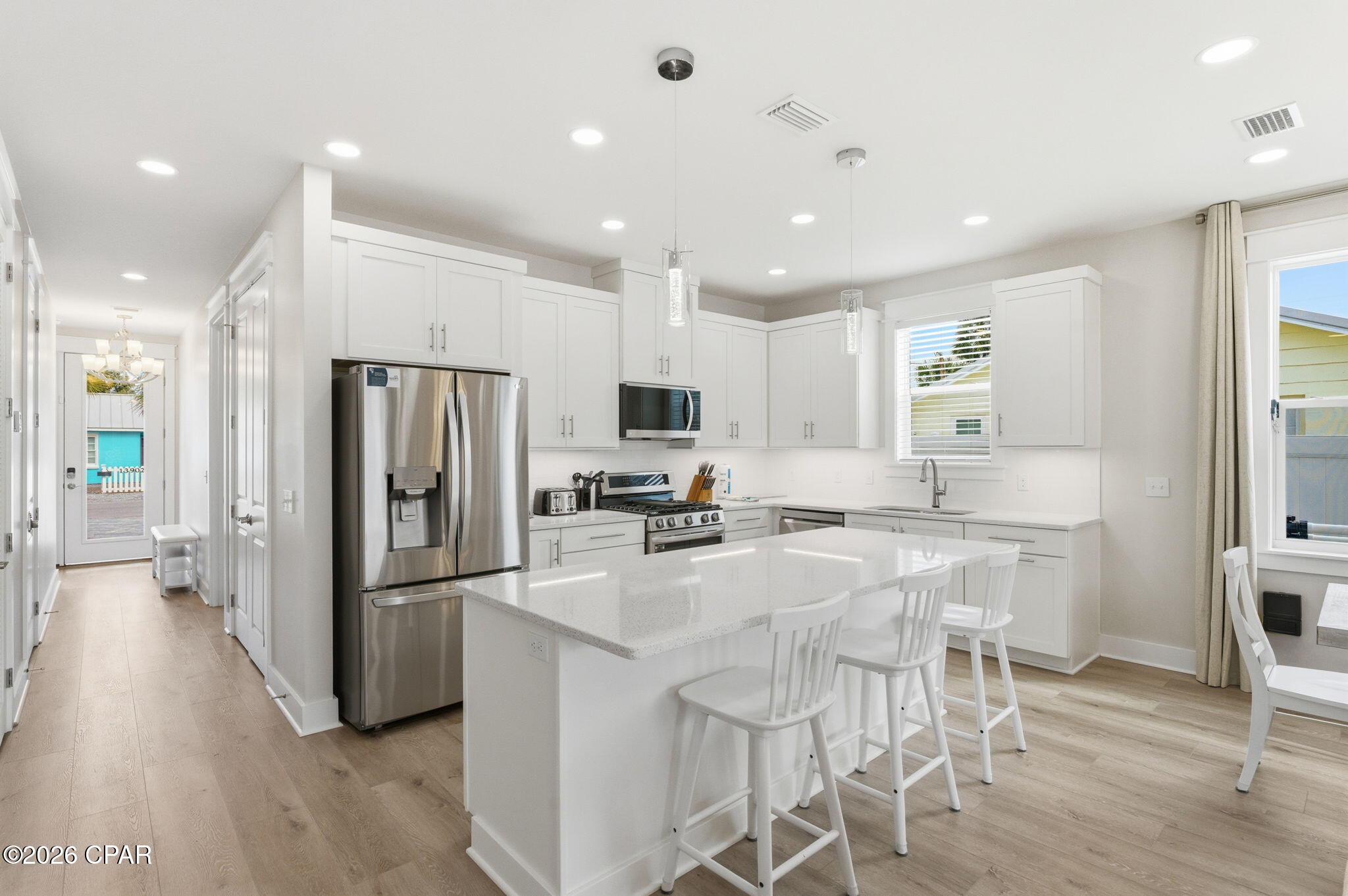 Bright white kitchen with stainless steel appliances and a large island lined with bar stools.