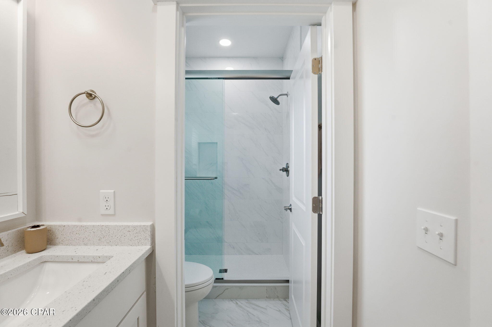 Bathroom with a glass-enclosed marble-look shower and speckled quartz vanity.
