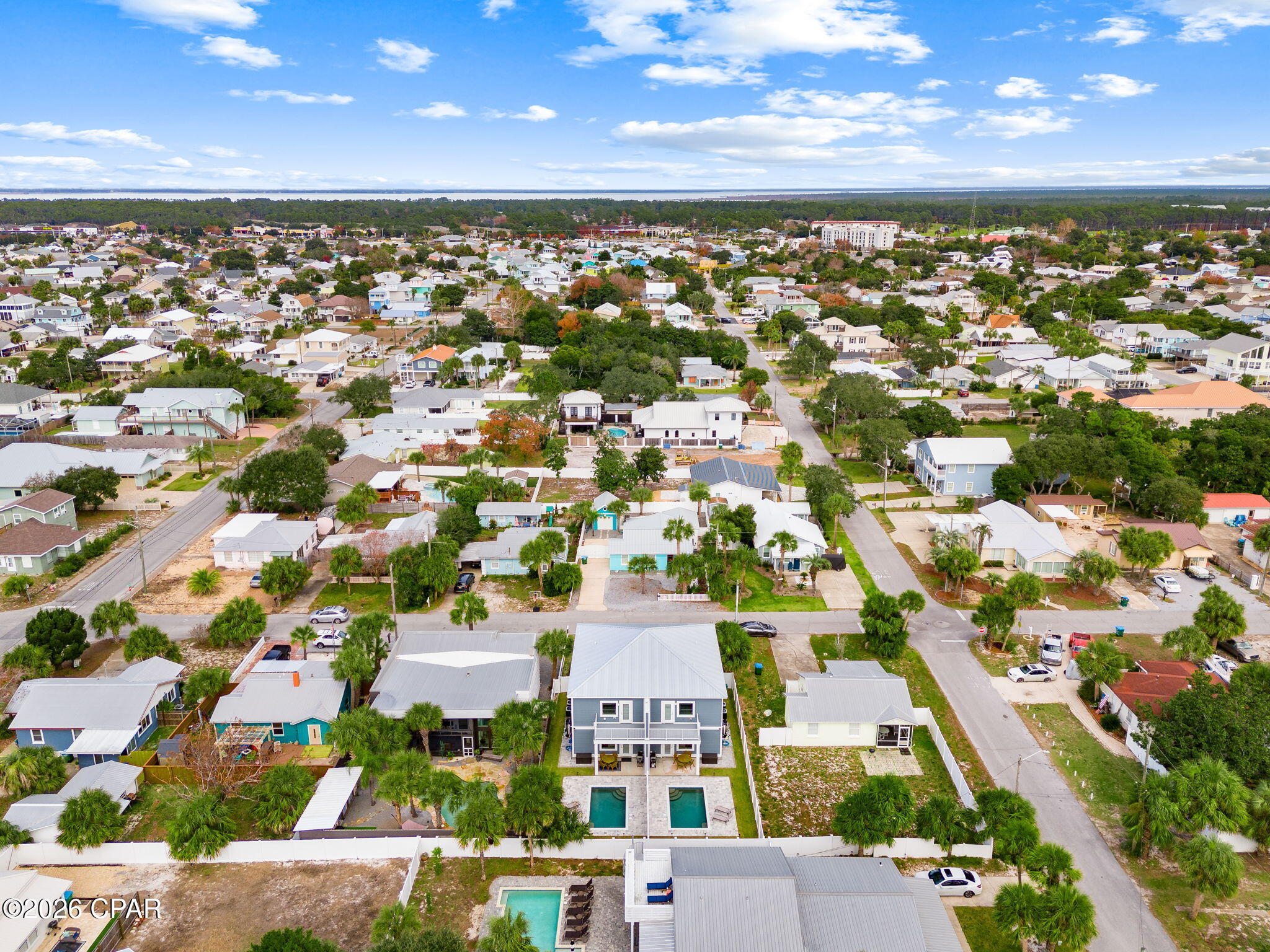 Aerial view of a blue two-story property with twin pools, surrounded by homes near the coast.