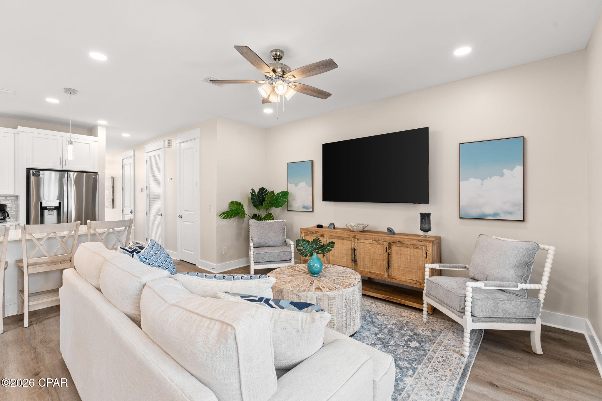 Furnished living room with a white sofa, gray armchairs, patterned rug, and open kitchen.