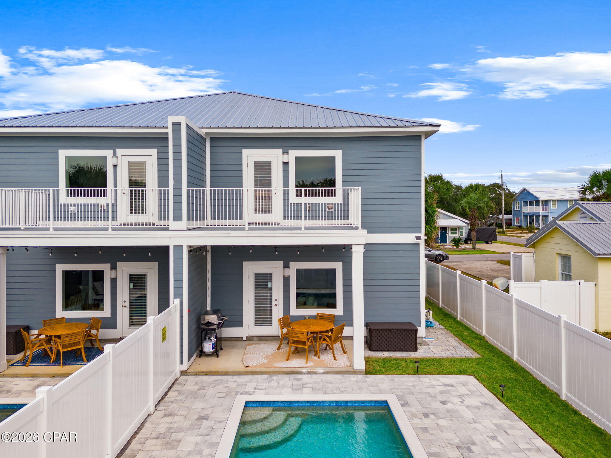 Blue-gray duplex with white balconies, furnished patios, and a small pool in the fenced yard.