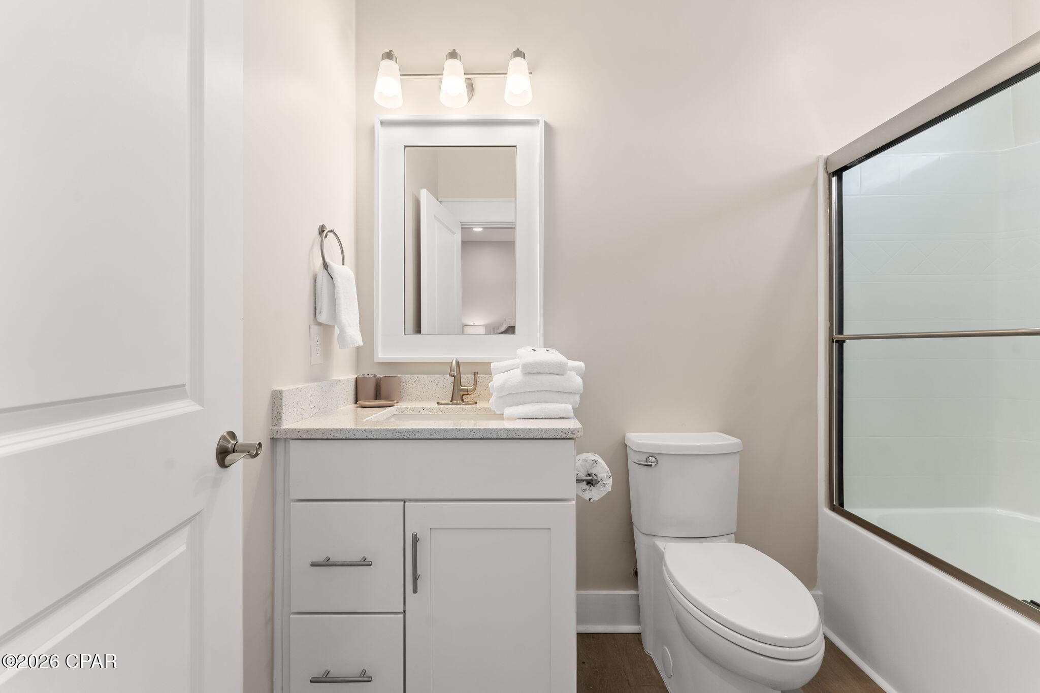 Bathroom with white vanity, stacked towels, toilet, and glass-enclosed tub and shower.
