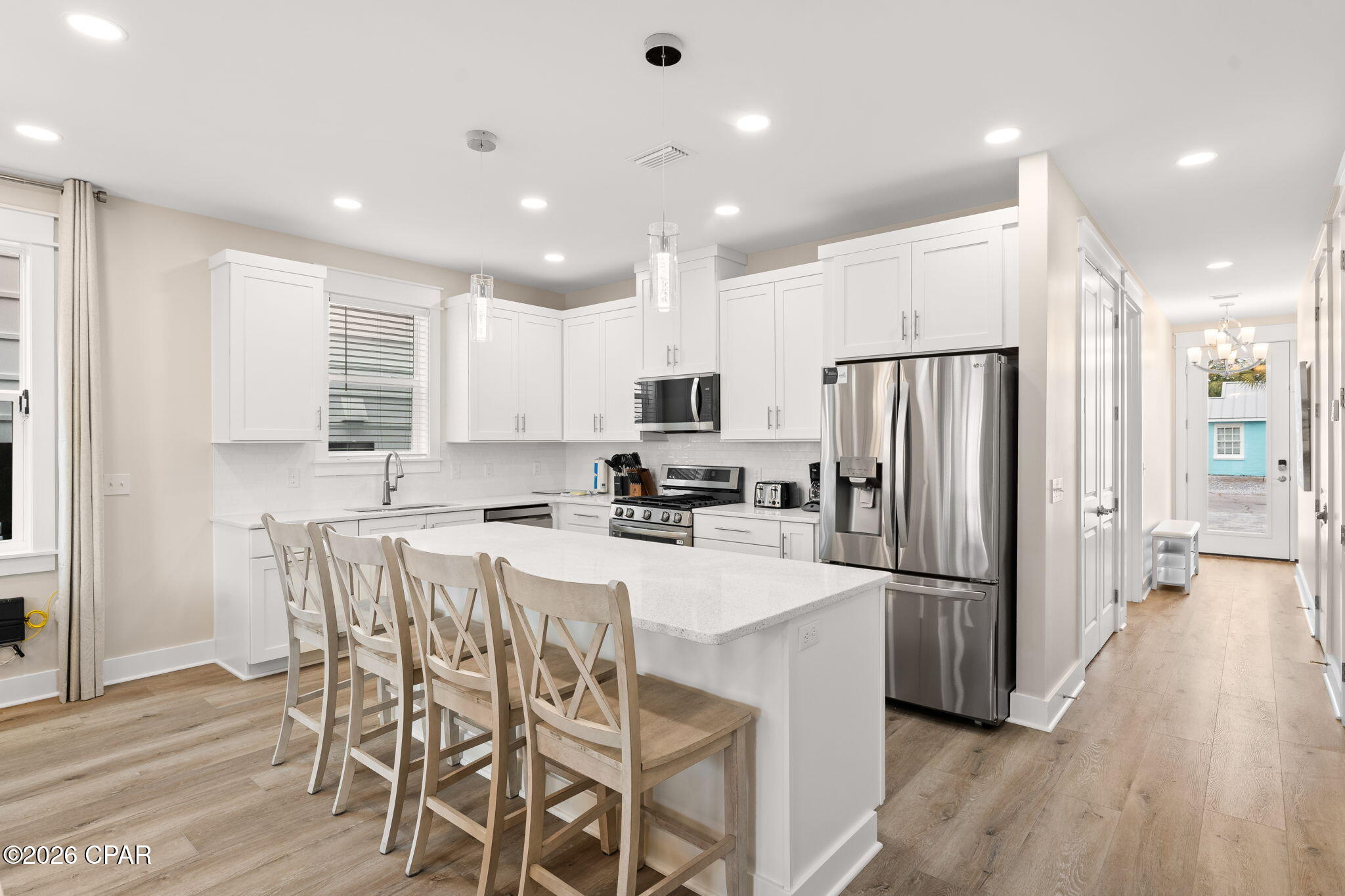 Bright kitchen with a large island, white cabinetry, stainless steel appliances, and light wood floors.
