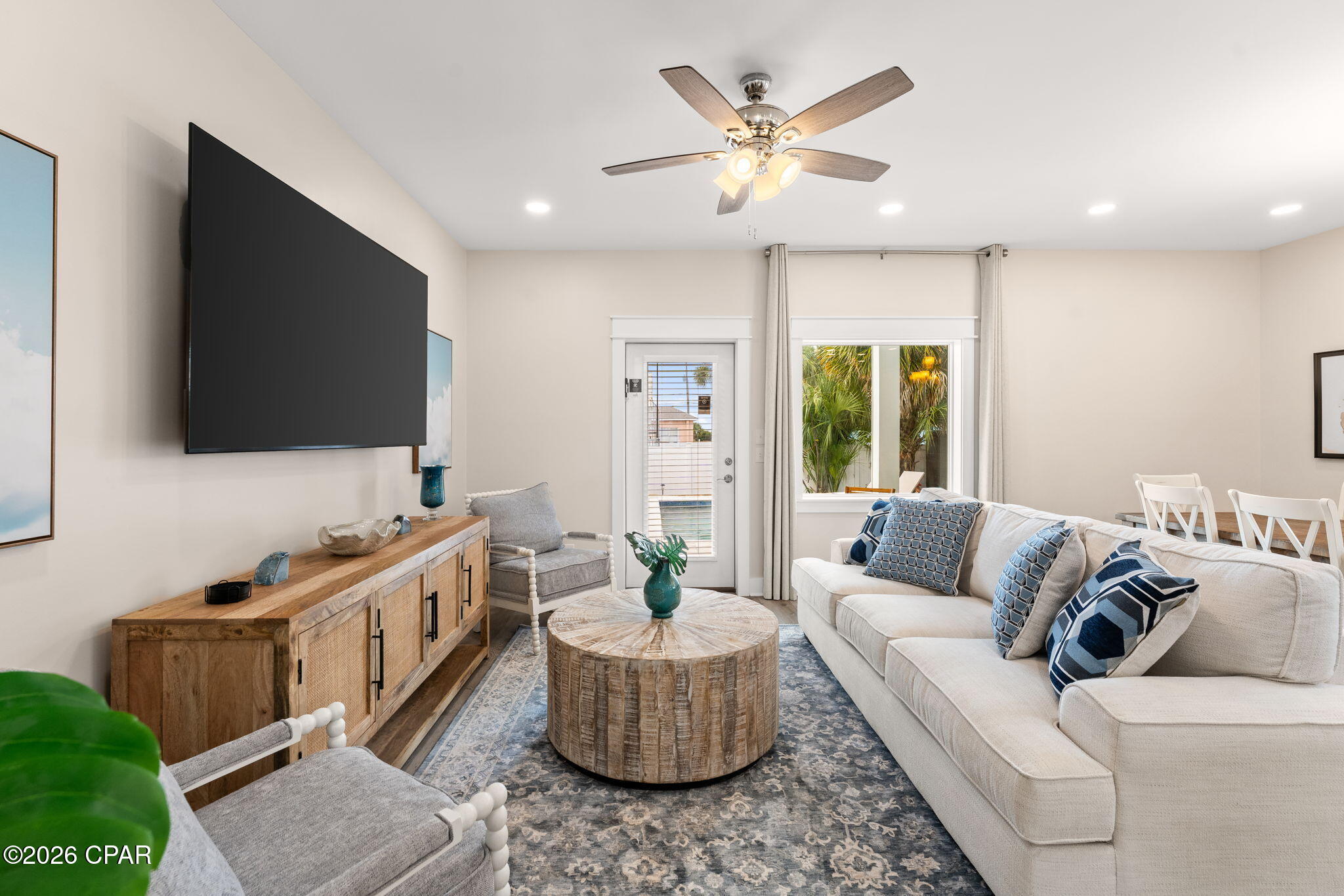 Furnished living room with a white sectional, round wood coffee table, and wall-mounted television.