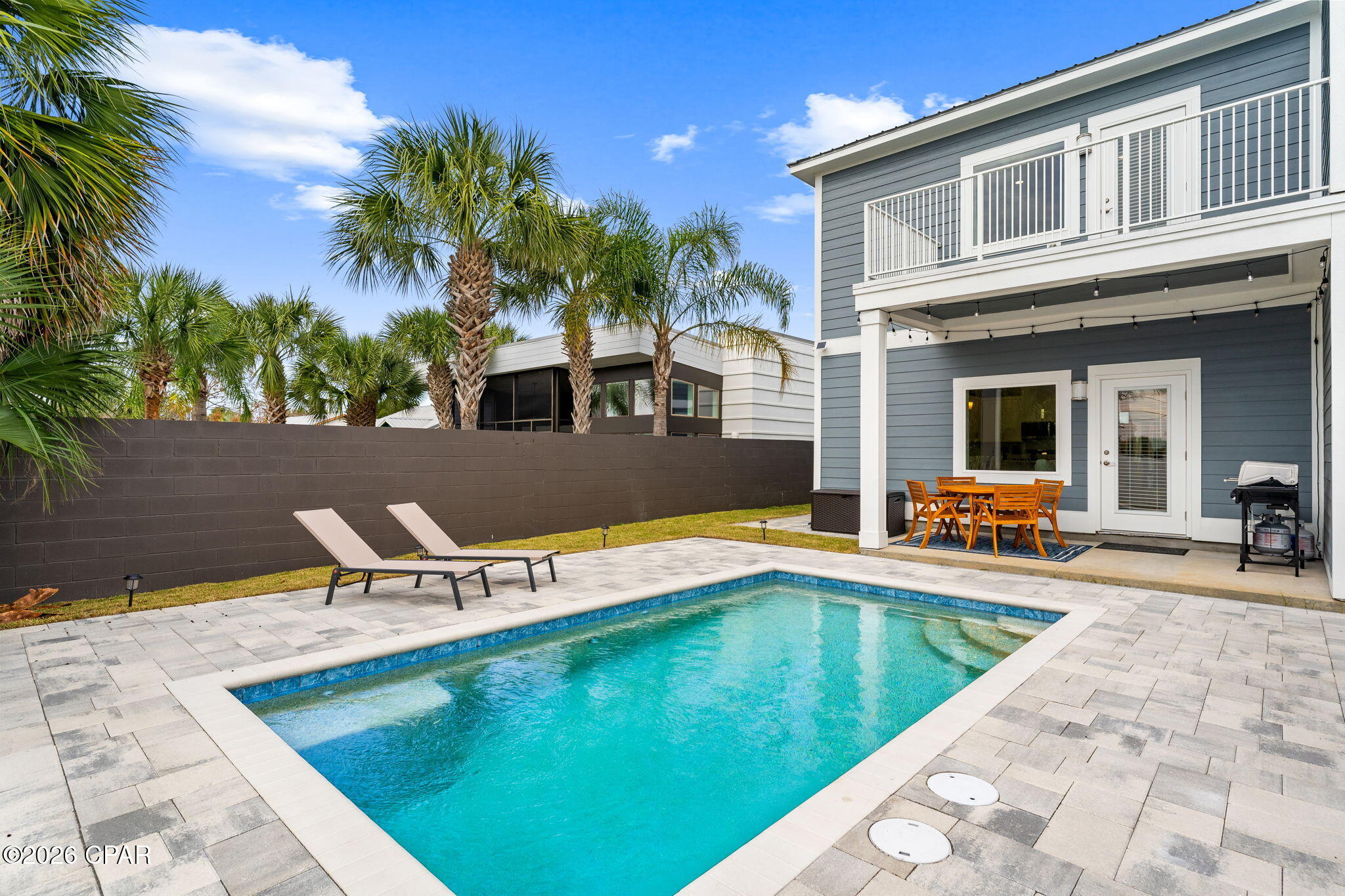 Private swimming pool beside a two-story blue home with a furnished patio.
