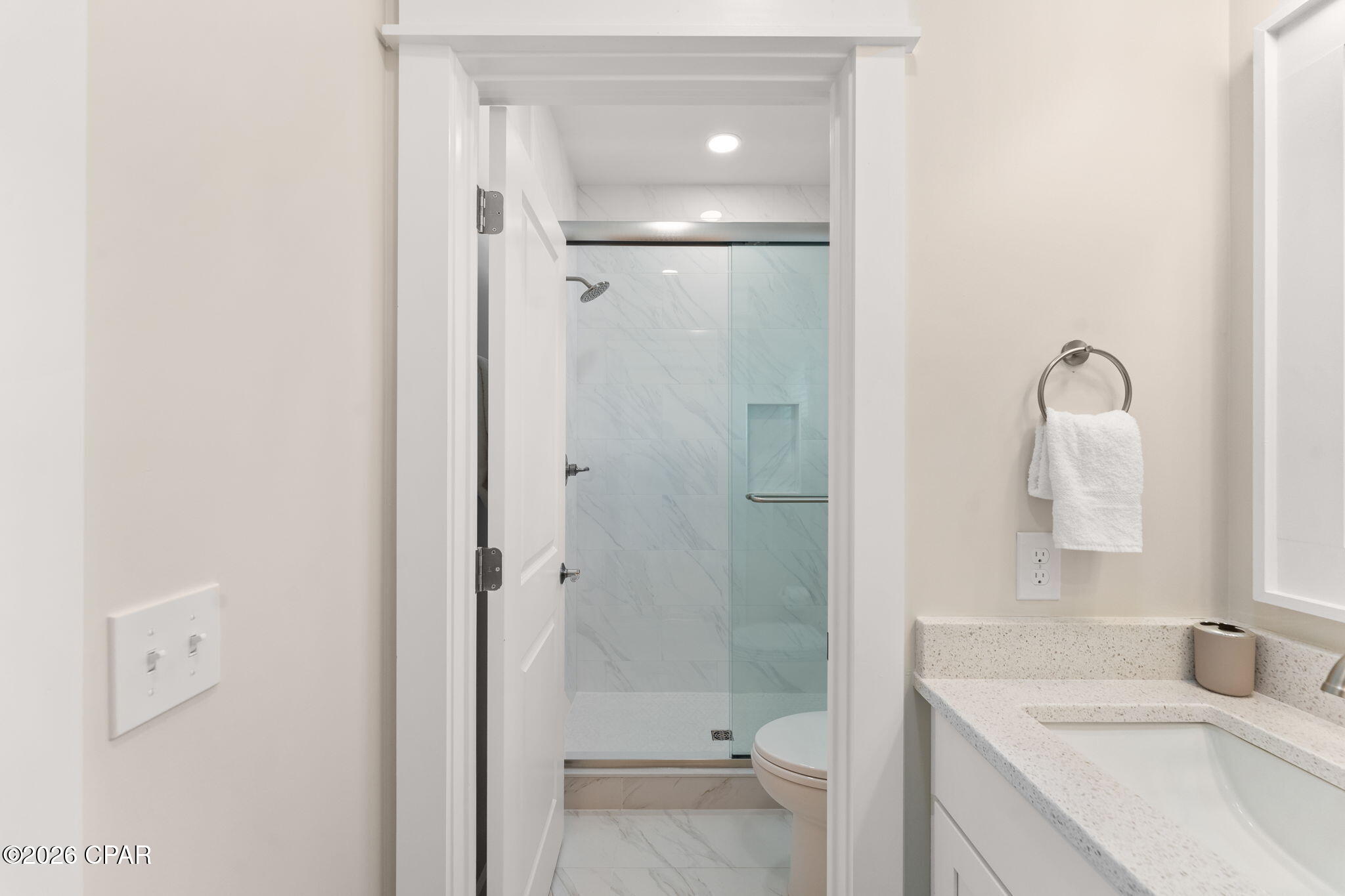 Bathroom with a glass shower, marble-look tile, and speckled vanity countertop.