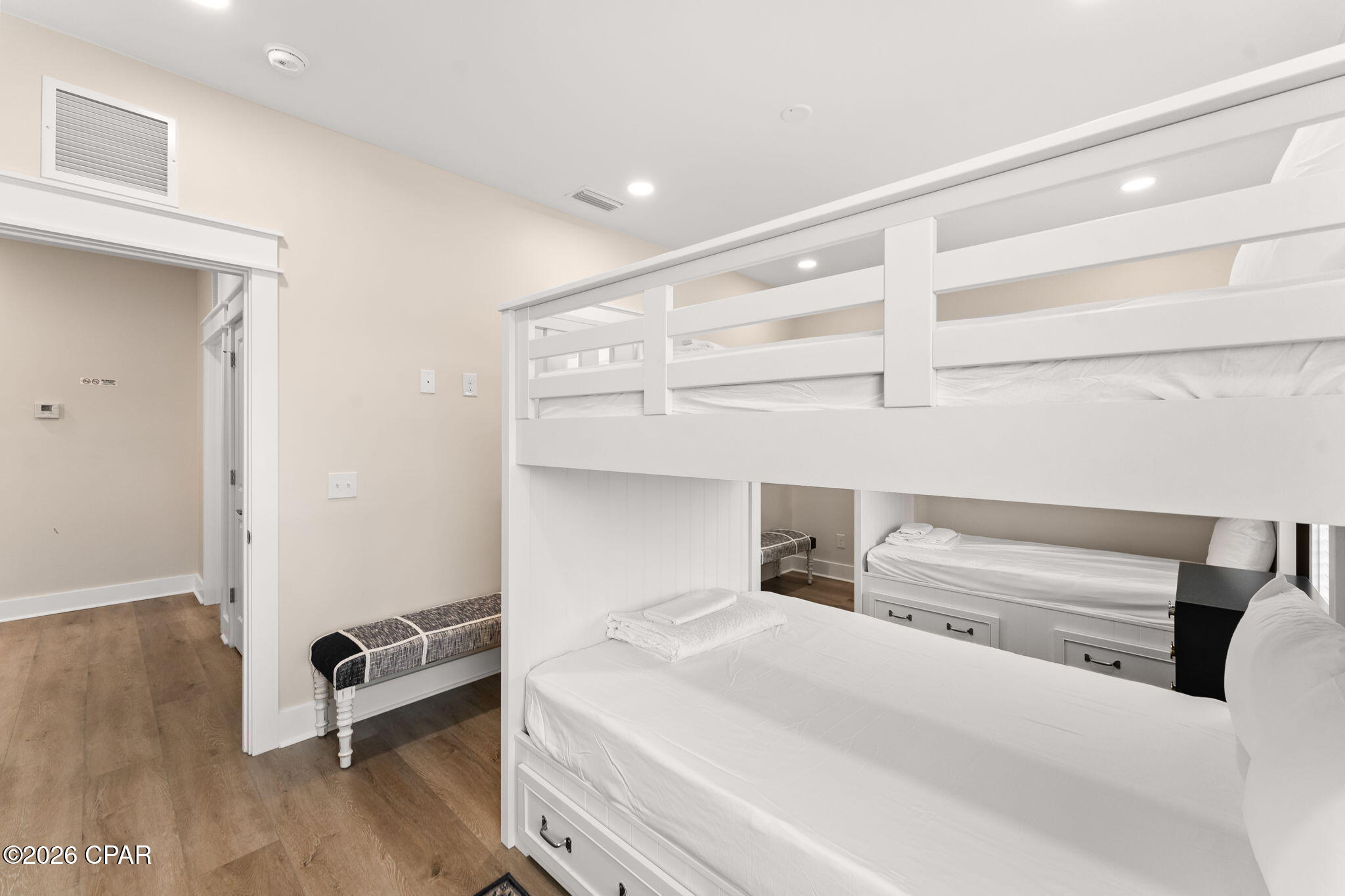 Bedroom with white built-in bunk beds, single beds, and wood-look flooring.