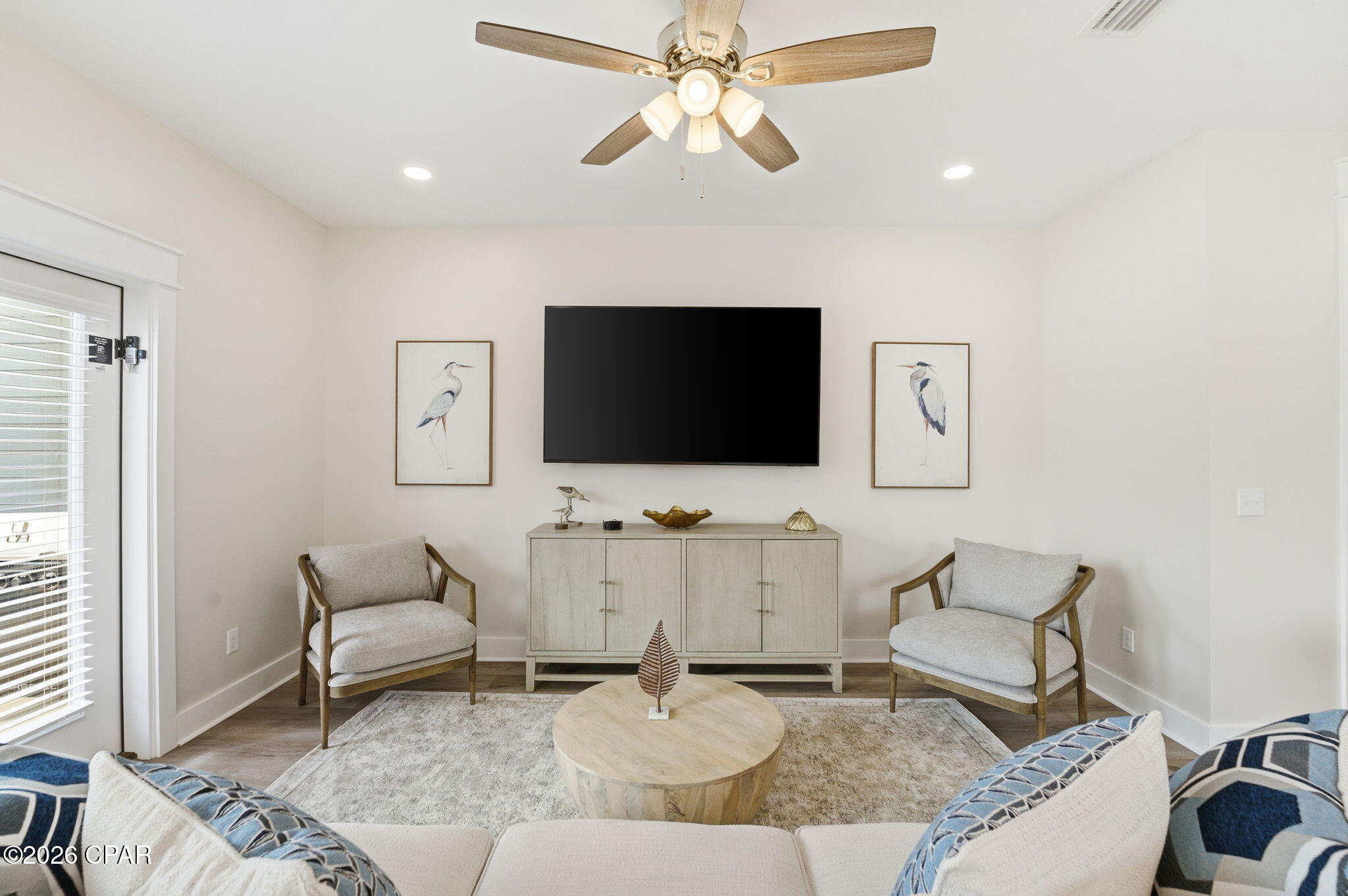 Furnished living room with a wall-mounted TV, matching armchairs, round coffee table, and framed bird prints.