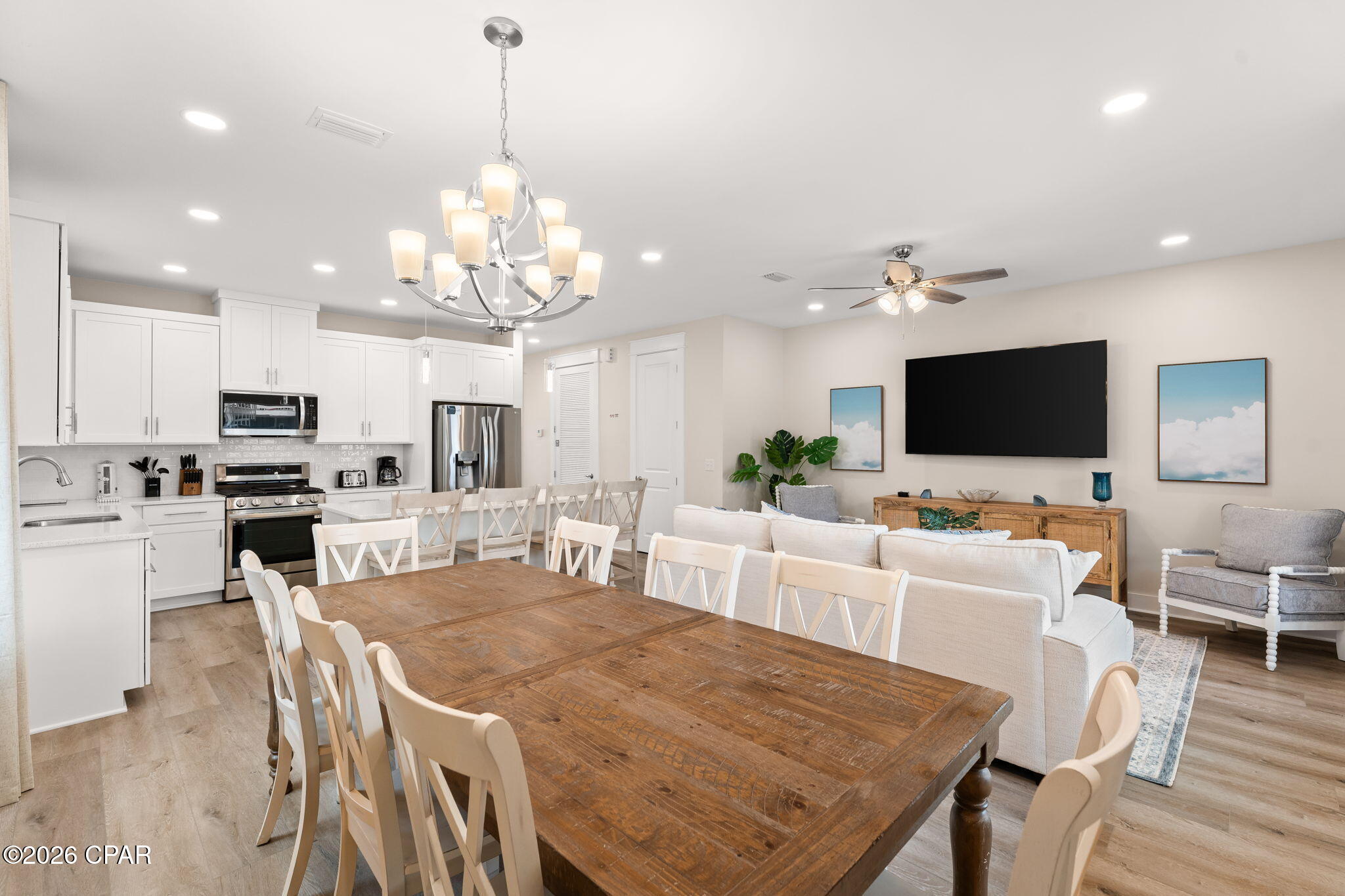 Open-plan kitchen and living area with white cabinets, stainless appliances, and a large rustic dining table.