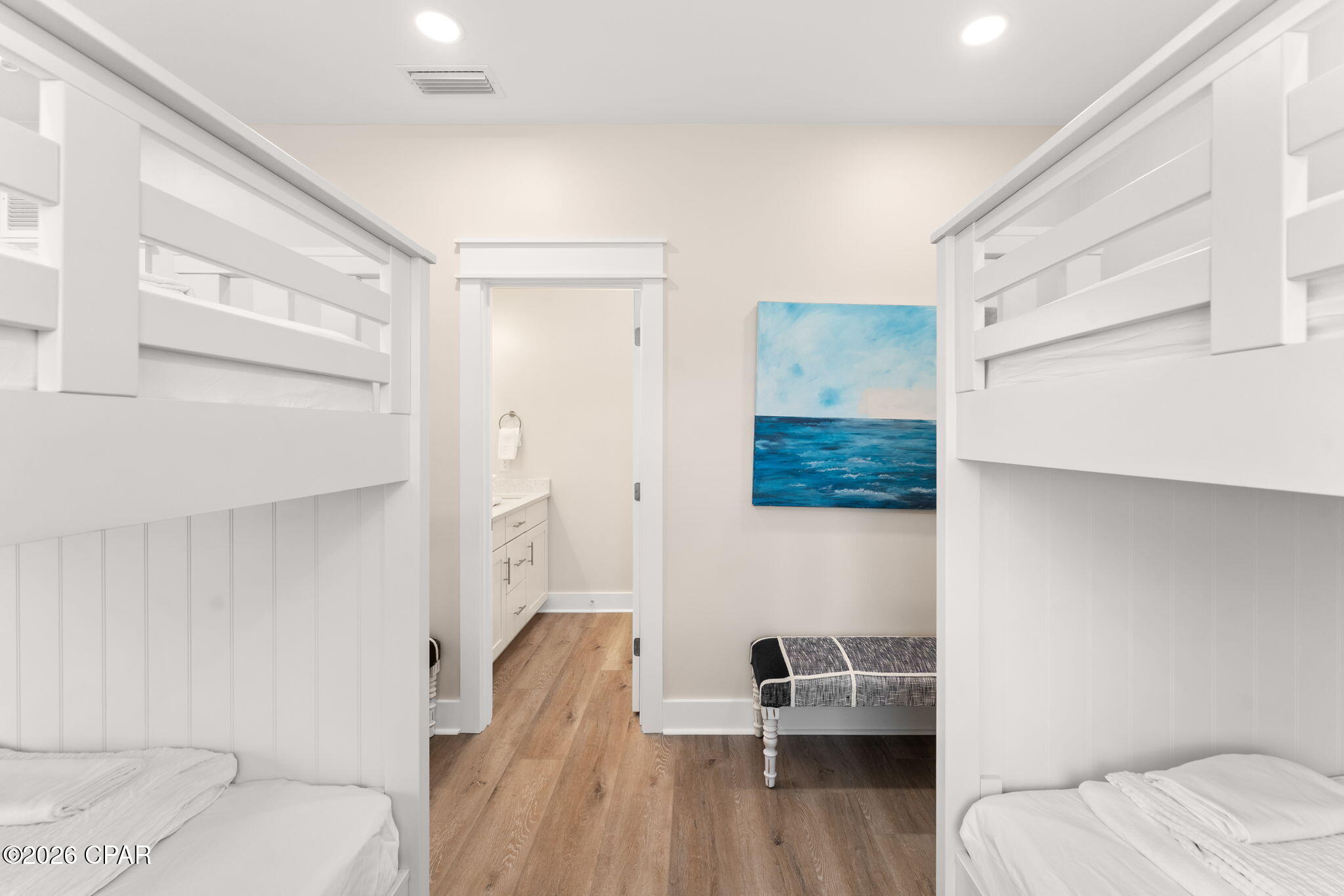 Bedroom with white built-in bunk beds, wood-look floors, and blue ocean artwork.
