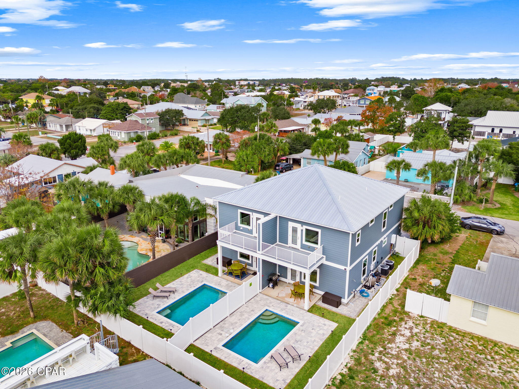 Aerial view of a blue two-story home with a metal roof and two fenced swimming pools.