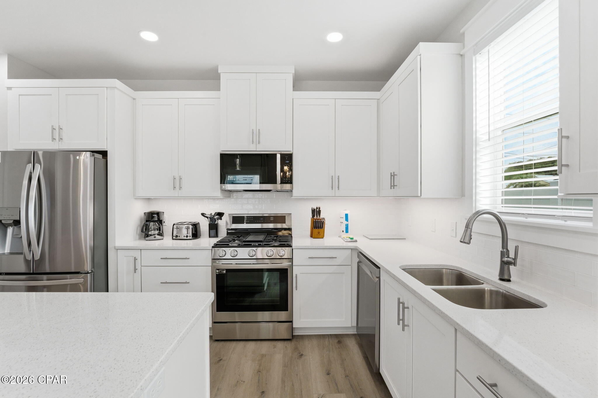 Bright white kitchen with stainless steel appliances, a gas range, and a double-basin sink beneath a window.