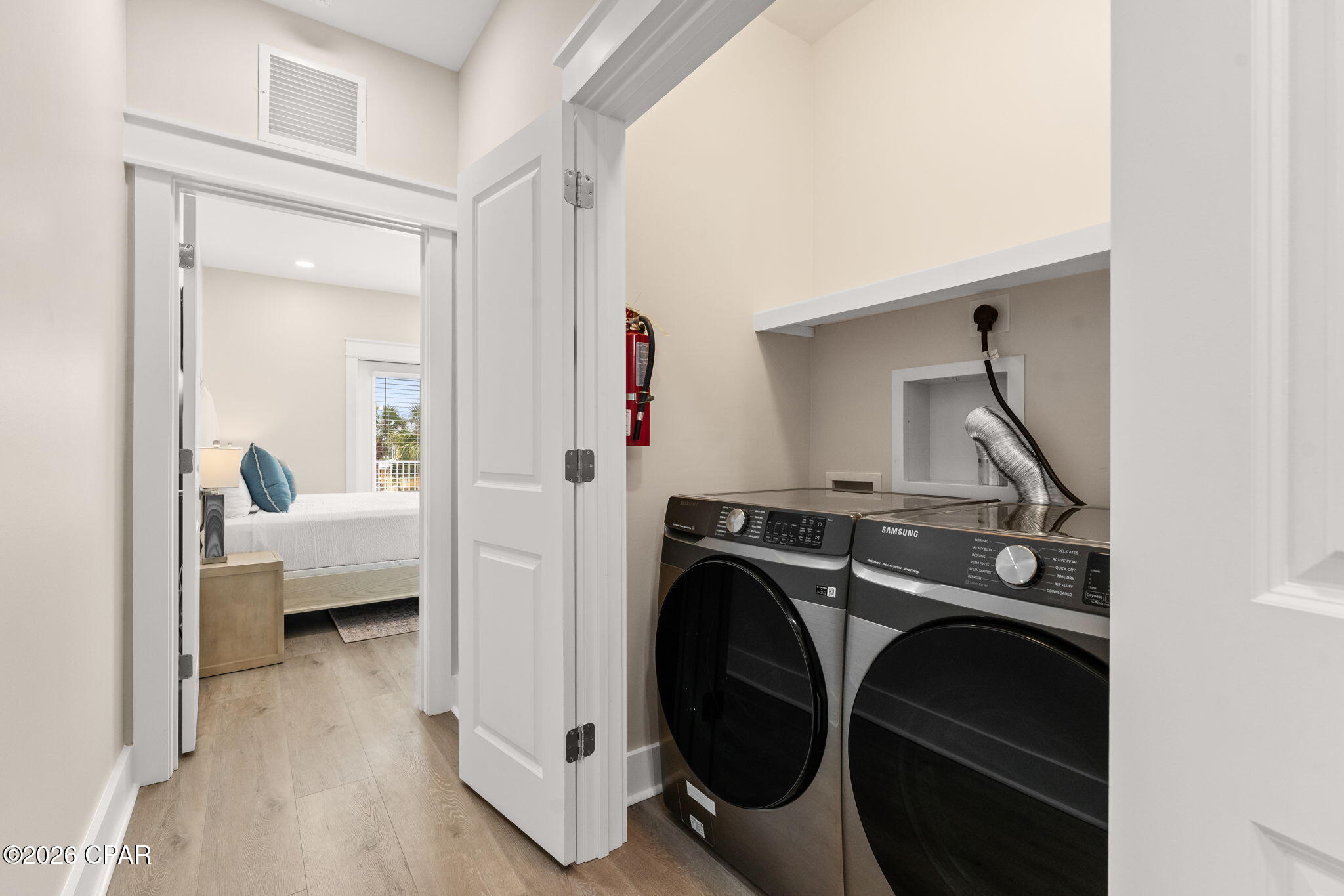 Laundry room with front-loading washer and dryer beside an open doorway to a bedroom.