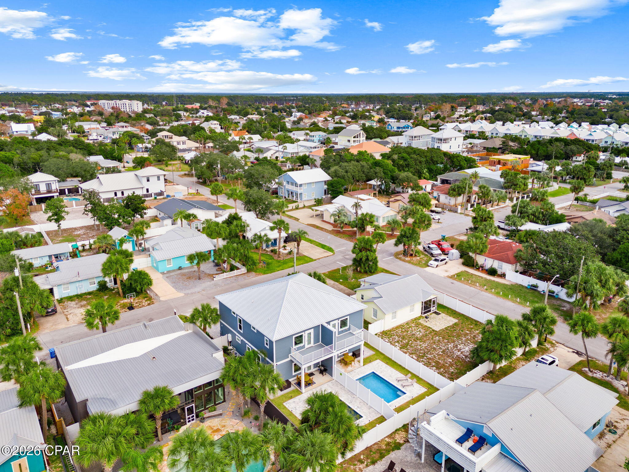 Aerial view of a blue two-story home with a fenced pool among palm-lined streets.