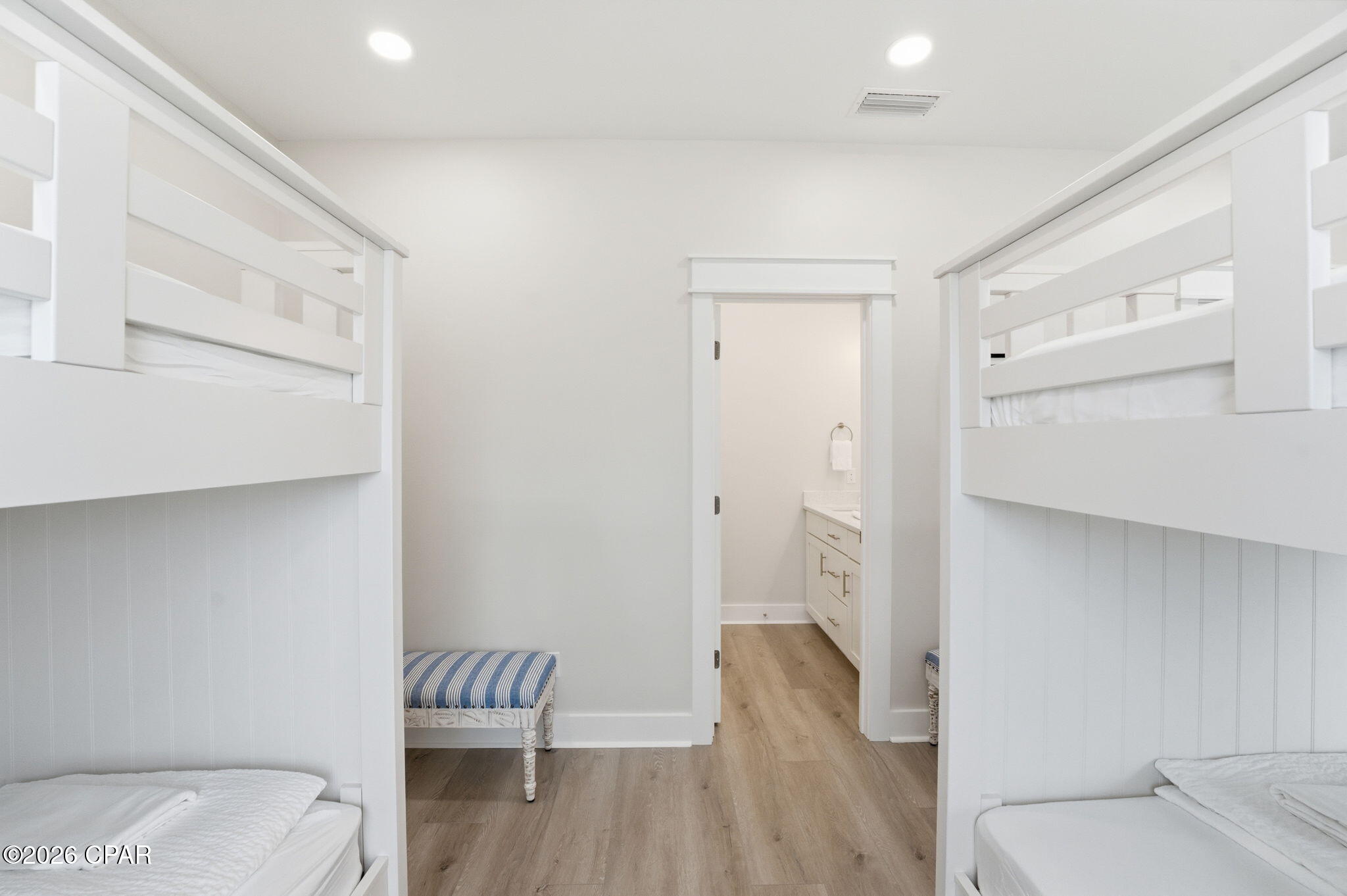 Bedroom with white bunk beds on both sides and an open doorway to a bathroom vanity.
